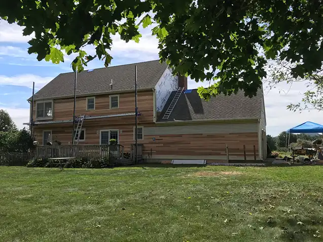 House undergoing siding replacement with cedar clapboards and construction tools in the yard.