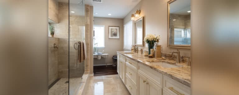 Elegant Connecticut bathroom remodel featuring a frameless glass shower, double vanity with granite countertops, gold fixtures, and soft lighting—example of a modern bathroom renovation by Authentic Renovations.